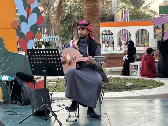 A live music performance at the Jood Market in Prince Saud Park in Dhahran, Eastern Province, Saudi Arabia, an open community market that supports local projects, artisanal products, and homemade foods, outdoor shopping corners, family events, and recreational activities, with a vibrant heritage and social atmosphere.