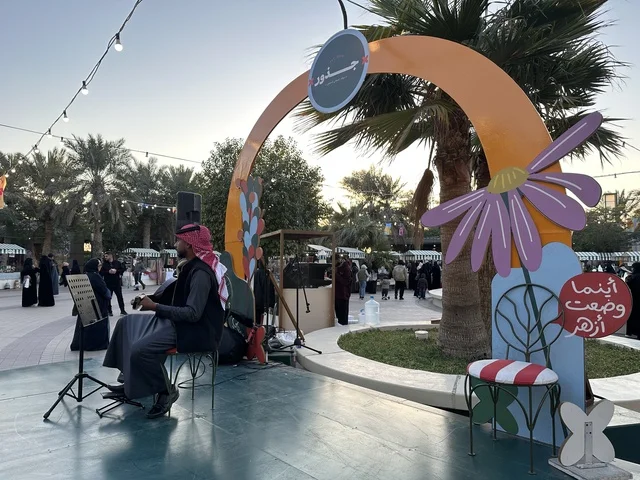 A live music performance at the Jood Market in Prince Saud Park in Dhahran, Eastern Province, Saudi Arabia, an open community market that supports local projects, artisanal products, and homemade foods, outdoor shopping corners, family events, and recreational activities, with a vibrant heritage and social atmosphere.