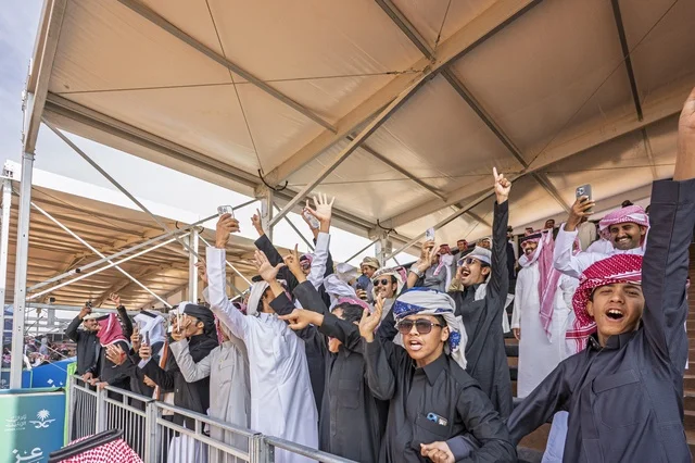 Expressions of enthusiasm and wide participation from camel owners, King Abdulaziz Camel Festival, Kingdom of Saudi Arabia, a major national heritage event, competitions and beauty of camels, shows and auctions, cultural and heritage activities, festive atmosphere reflecting the authenticity of the Saudi heritage.
