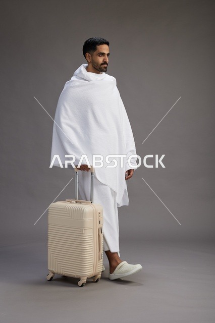 A Saudi Arabian Gulf man in Ihram clothing with a travel bag, going to Mecca to perform the rituals of Hajj and Umrah, full-body, gray background.