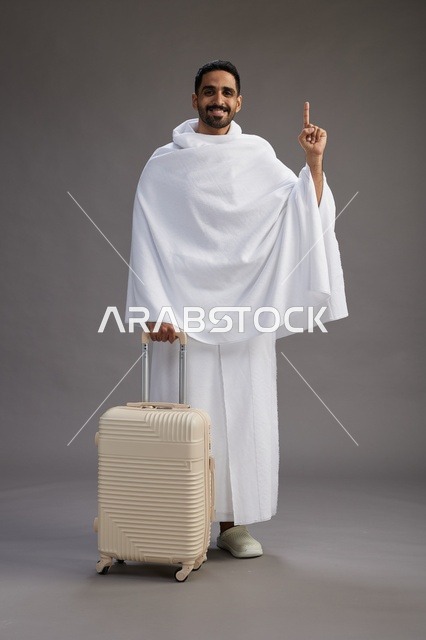 A Saudi Arabian Gulf man in Ihram clothing with a travel bag, going to Mecca to perform the rituals of Hajj and Umrah, full-body, gray background.