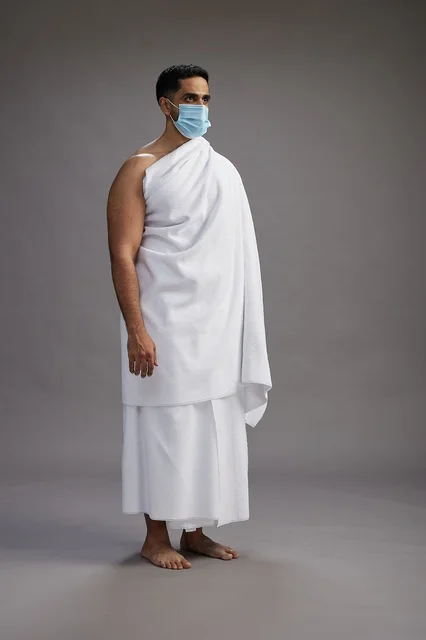 رجل عربي  سعودي  خليجي بملابس الإحرام يرتدي كمامة واقف استعدادًا للحج, الوقايه من فايروس كورونا, كامل الجسم, خلفيه رماديه