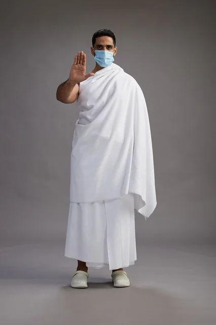 رجل عربي  سعودي  خليجي بملابس الإحرام يرتدي كمامة واقف استعدادًا للحج, الوقايه من فايروس كورونا, كامل الجسم, خلفيه رماديه