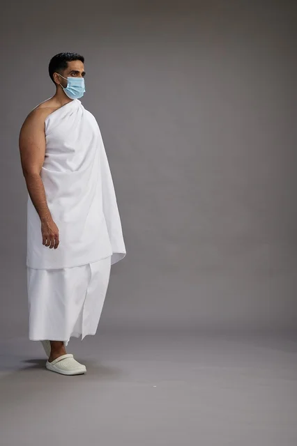 رجل عربي  سعودي  خليجي بملابس الإحرام يرتدي كمامة واقف استعدادًا للحج, الوقايه من فايروس كورونا, كامل الجسم, خلفيه رماديه