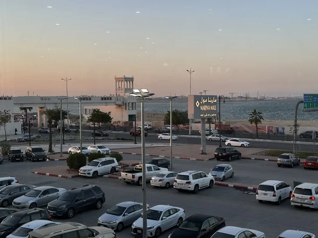 وقوف السيارات في الباركينج الخارجي لمارينا مول في مدينة الدمام، المنطقة الشرقية، المملكة العربية السعودية، مركز تسوق وترفيه مطل على الواجهة البحرية، متاجر وعلامات تجارية متنوعة، مطاعم ومقاهي بإطلالات بحرية، مرافق ترفيهية وخدمية، وجهة عائلية تجمع التسوق والترفيه