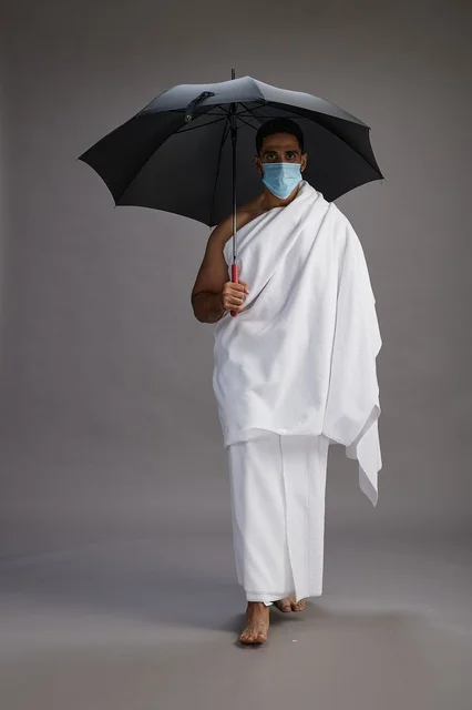 بورتريه لحاج  عربي سعودي  خليجي بملابس الإحرام يحمل مظلة ويرتدي كمامة, الوقايه من كوفيد 19, كامل الجسم, خلفيه رماديه
