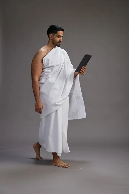 بورتريه لحاج سعودي بملابس الإحرام يحمل تابلت, الاستعداد لاداء مناسك الحج والعمره, كامل الجسم, خلفيه رماديه
