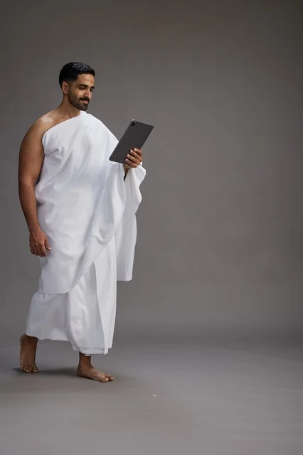 بورتريه لحاج سعودي بملابس الإحرام يحمل تابلت, الاستعداد لاداء مناسك الحج والعمره, كامل الجسم, خلفيه رماديه