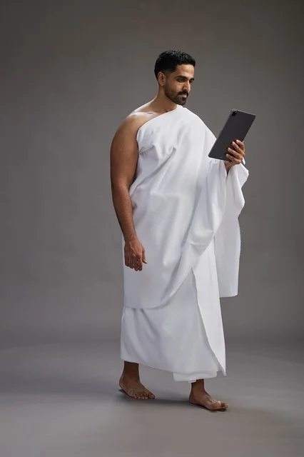 بورتريه لحاج سعودي بملابس الإحرام يحمل تابلت, الاستعداد لاداء مناسك الحج والعمره, كامل الجسم, خلفيه رماديه