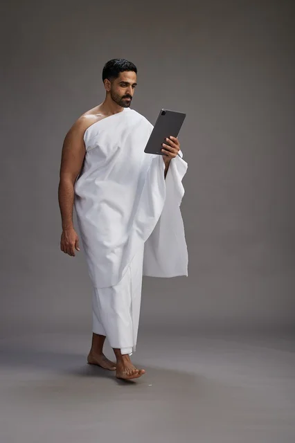 بورتريه لحاج سعودي بملابس الإحرام يحمل تابلت, الاستعداد لاداء مناسك الحج والعمره, كامل الجسم, خلفيه رماديه