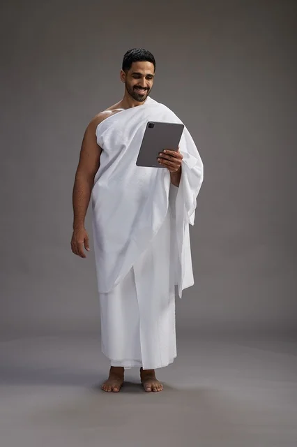 بورتريه لحاج سعودي بملابس الإحرام يحمل تابلت, الاستعداد لاداء مناسك الحج والعمره, كامل الجسم, خلفيه رماديه