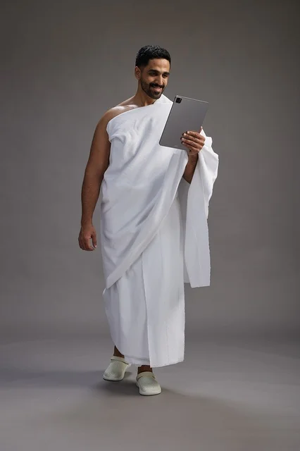 بورتريه لحاج سعودي بملابس الإحرام يحمل تابلت, الاستعداد لاداء مناسك الحج والعمره, كامل الجسم, خلفيه رماديه