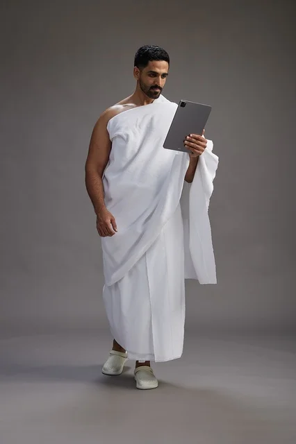 بورتريه لحاج سعودي بملابس الإحرام يحمل تابلت, الاستعداد لاداء مناسك الحج والعمره, كامل الجسم, خلفيه رماديه