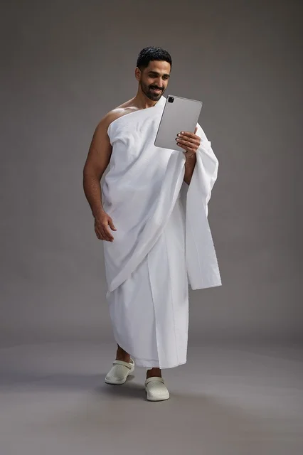 بورتريه لحاج سعودي بملابس الإحرام يحمل تابلت, الاستعداد لاداء مناسك الحج والعمره, كامل الجسم, خلفيه رماديه