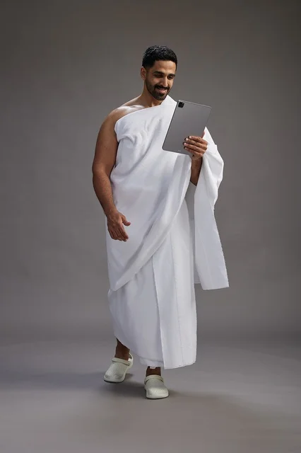بورتريه لحاج سعودي بملابس الإحرام يحمل تابلت, الاستعداد لاداء مناسك الحج والعمره, كامل الجسم, خلفيه رماديه