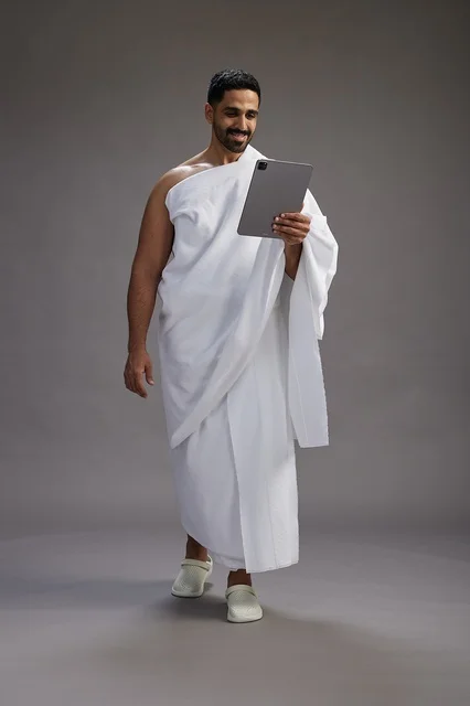 بورتريه لحاج سعودي بملابس الإحرام يحمل تابلت, الاستعداد لاداء مناسك الحج والعمره, كامل الجسم, خلفيه رماديه