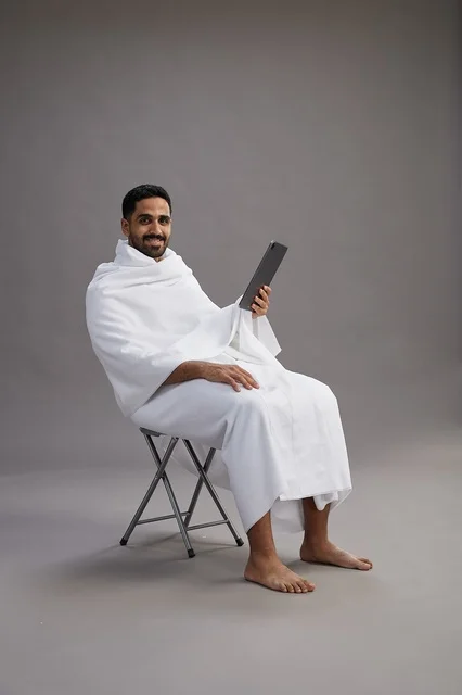 بورتريه لحاج سعودي بملابس الإحرام يحمل تابلت ويجلس على كرسي, الاستعداد لاداء مناسك الحج والعمره, خلفيه رماديه بورتريه لحاج سعودي بملابس الإحرام يحمل تابلت ويجلس على كرسي, الاستعداد لاداء مناسك الحج والعمره, خلفيه رماديه