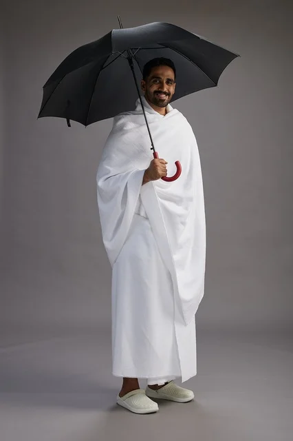 بورتريه لحاج  عربي سعودي  خليجي بملابس الإحرام يحمل مظله, الذهاب لاداء مناسك الحج والعمره,  كامل الجسم, خلفيه رماديه