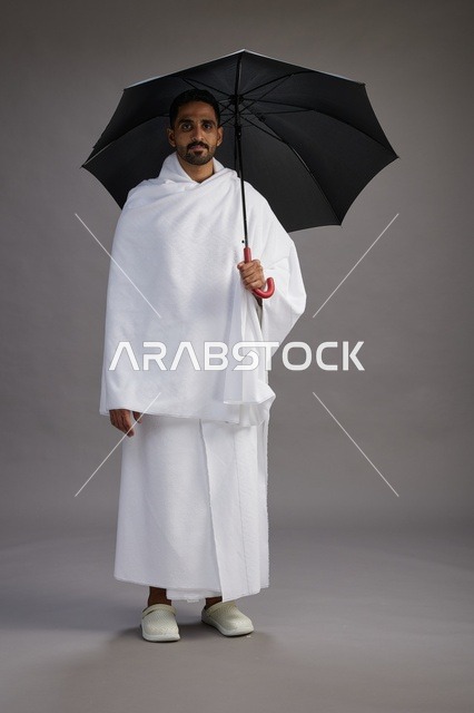 بورتريه لحاج  عربي سعودي  خليجي بملابس الإحرام يحمل مظله, الذهاب لاداء مناسك الحج والعمره,  كامل الجسم, خلفيه رماديه