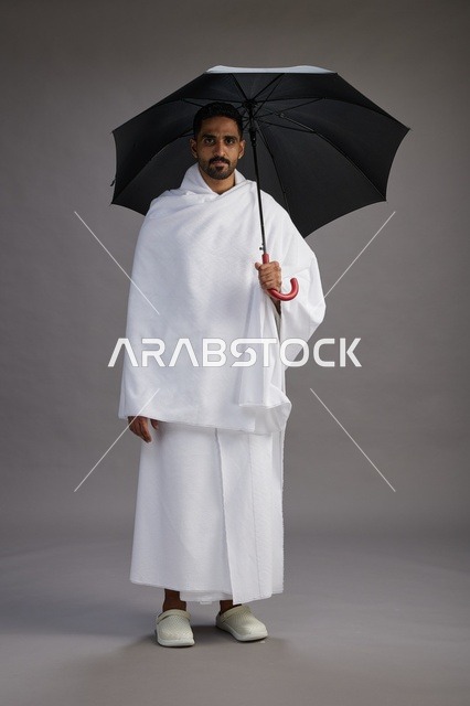 بورتريه لحاج  عربي سعودي  خليجي بملابس الإحرام يحمل مظله, الذهاب لاداء مناسك الحج والعمره,  كامل الجسم, خلفيه رماديه