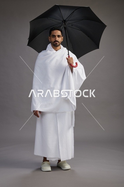 بورتريه لحاج  عربي سعودي  خليجي بملابس الإحرام يحمل مظله, الذهاب لاداء مناسك الحج والعمره,  كامل الجسم, خلفيه رماديه