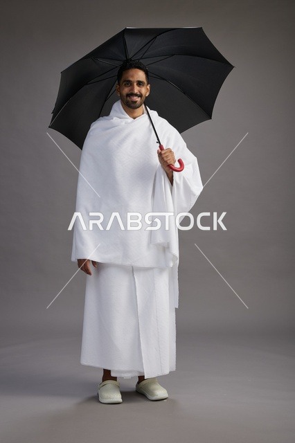 بورتريه لحاج  عربي سعودي  خليجي بملابس الإحرام يحمل مظله, الذهاب لاداء مناسك الحج والعمره,  كامل الجسم, خلفيه رماديه