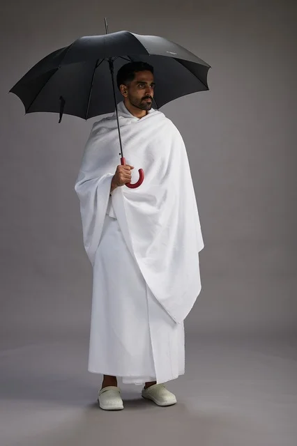 بورتريه لحاج  عربي سعودي  خليجي بملابس الإحرام يحمل مظله, الذهاب لاداء مناسك الحج والعمره,  كامل الجسم, خلفيه رماديه
