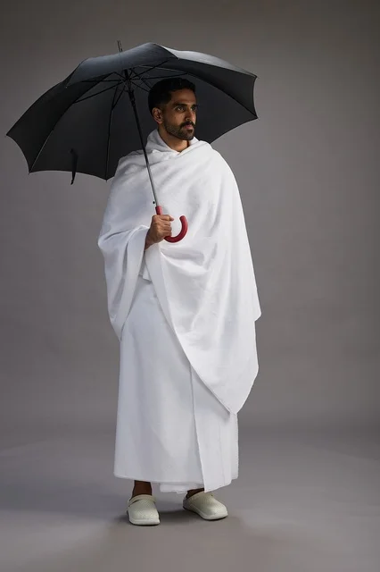 بورتريه لحاج  عربي سعودي  خليجي بملابس الإحرام يحمل مظله, الذهاب لاداء مناسك الحج والعمره,  كامل الجسم, خلفيه رماديه