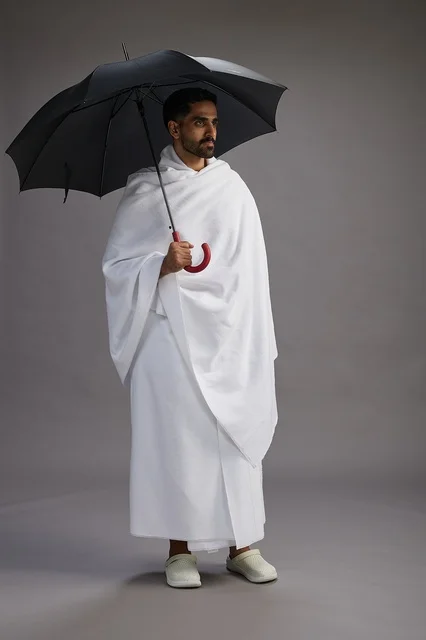 بورتريه لحاج  عربي سعودي  خليجي بملابس الإحرام يحمل مظله, الذهاب لاداء مناسك الحج والعمره,  كامل الجسم, خلفيه رماديه