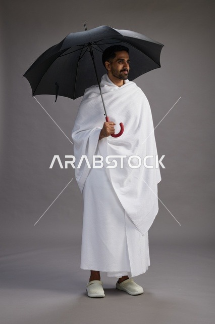 بورتريه لحاج  عربي سعودي  خليجي بملابس الإحرام يحمل مظله, الذهاب لاداء مناسك الحج والعمره,  كامل الجسم, خلفيه رماديه