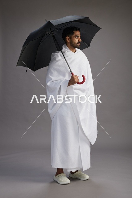بورتريه لحاج  عربي سعودي  خليجي بملابس الإحرام يحمل مظله, الذهاب لاداء مناسك الحج والعمره,  كامل الجسم, خلفيه رماديه