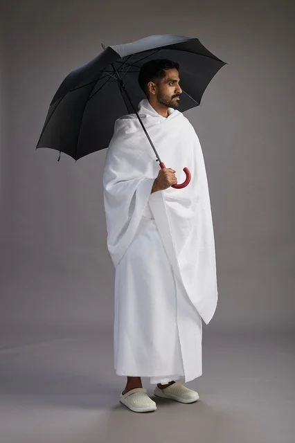 بورتريه لحاج  عربي سعودي  خليجي بملابس الإحرام يحمل مظله, الذهاب لاداء مناسك الحج والعمره,  كامل الجسم, خلفيه رماديه