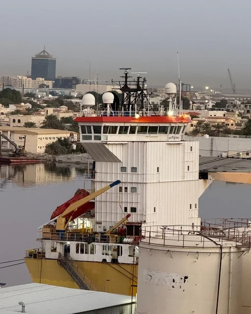 البواخر في ميناء عجمان صباحا، دولة الإمارات العربية المتحدة، مشهد بحري هادئ يعكس بداية يوم جديد، ألوان السماء الدافئة تنعكس على سطح البحر، حركة السفن في الميناء، أجواء صباحية ناعمة تجمع بين النشاط البحري والطبيعه