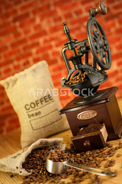 صورة لطاحونة قهوة قديمة تراثية على طاولة بخلفية حجر مع قهوه منثوره ، حبوب القهوه المتناثره ، حبوب البن المبعثره ، حبوب القهوه البنية العضويه ، بذور البن الطازجة ، طاحونة قهوة مصنوعة من الخشب بتصميم مميز