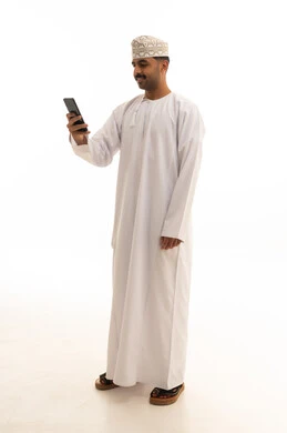 رجل عماني بالزي التقليدي يستخدم الهاتف الذكي