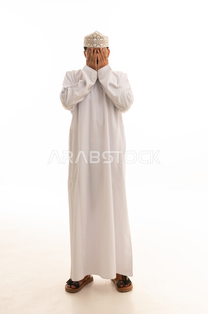رجل عماني بالدشداشة البيضاء يغطي وجهه
