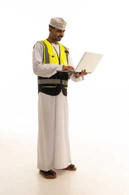 مهندس عماني بسترة السلامة يستخدم لابتوب بخلفية بيضاء