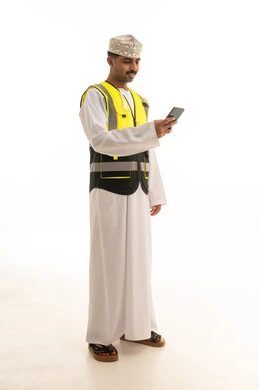 رجل عماني يرتدي سترة سلامة ويستخدم الجوال بخلفية بيضاء