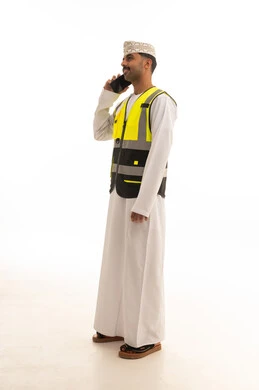رجل عُماني بسترة سلامة يتحدث بالهاتف خلفية بيضاء
