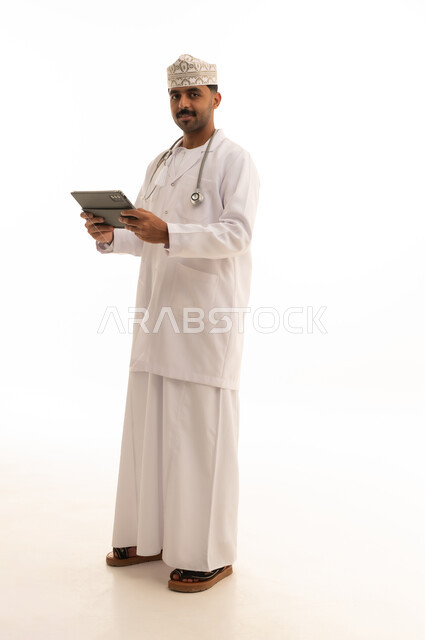 طبيب عماني يمسك جهاز لوحي بخلفية بيضاء