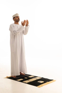 رجل عماني يصلي باللباس التقليدي بخلفية بيضاء