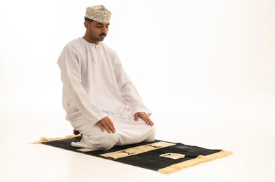 رجل عماني يصلي على السجادة خلفية بيضاء