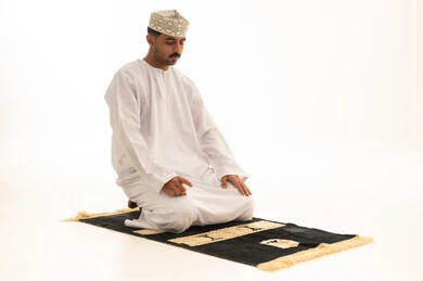 رجل عماني باللباس التقليدي يصلي على خلفية بيضاء
