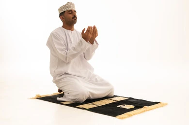 رجل عماني يدعو على سجادة الصلاة بخلفية بيضاء