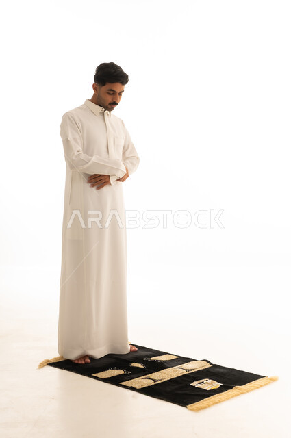 رجل سعودي يرتدي الثوب الأبيض يصلي على سجادة صلاة