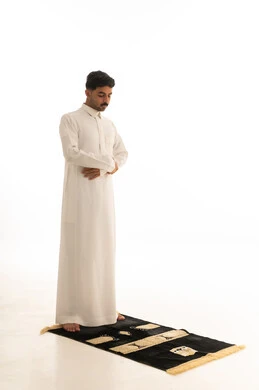 رجل سعودي بالثوب التقليدي يصلي على السجادة