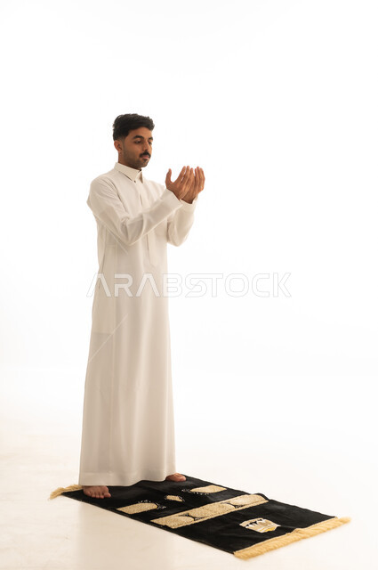 رجل سعودي بالثوب الأبيض يدعو على سجادة الصلاة