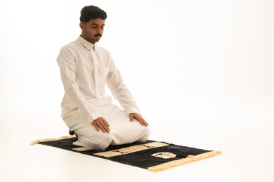 رجل سعودي يصلي بالثوب الأبيض على السجادة