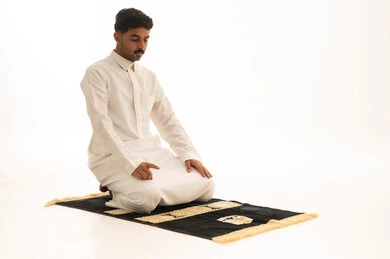 رجل سعودي يؤدي الصلاة على سجادة خلفية بيضاء