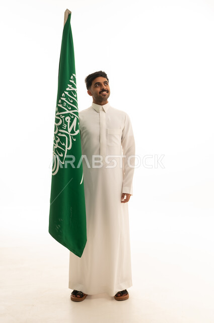 رجل سعودي بالثوب التقليدي مع علم المملكة